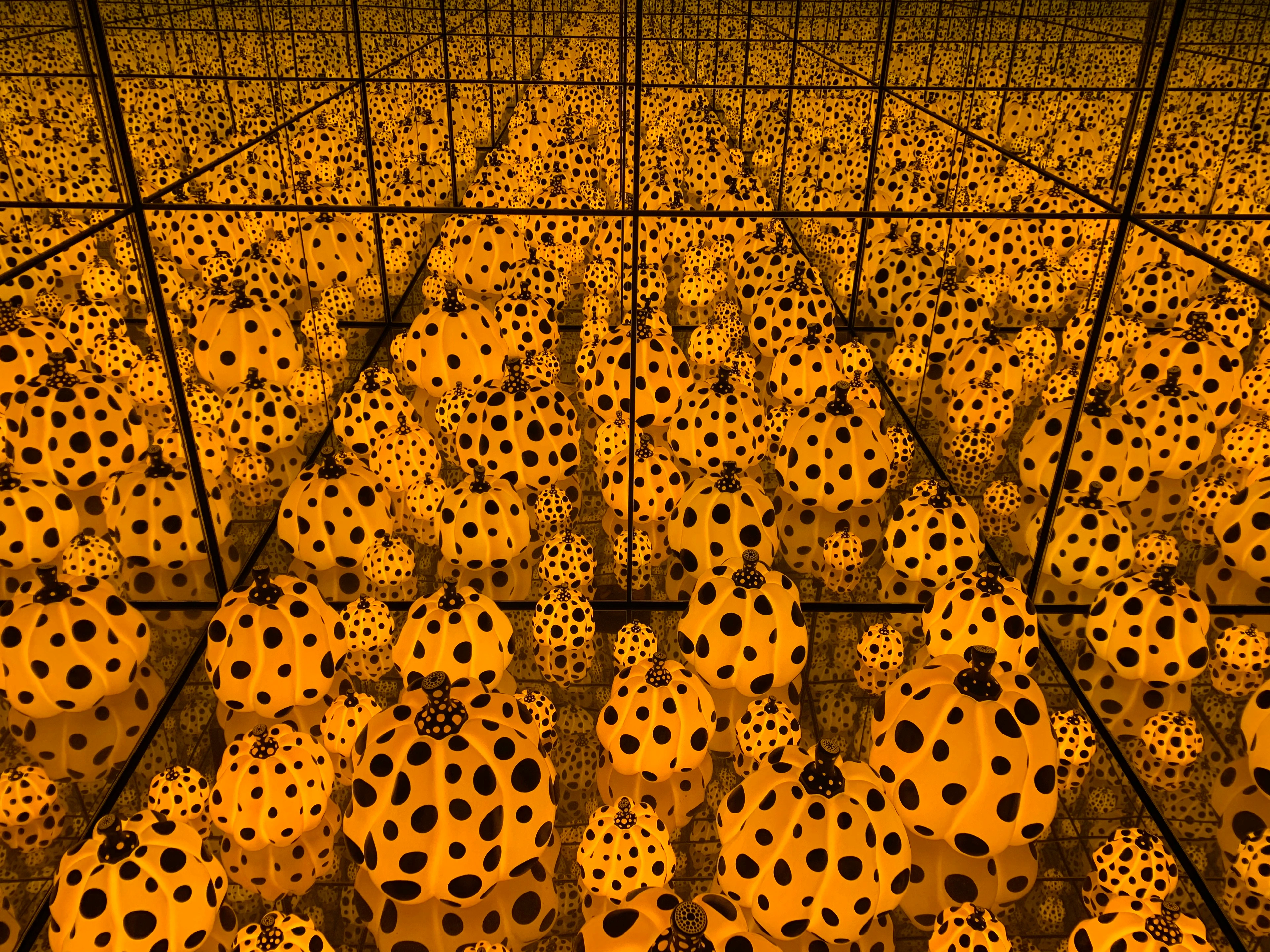 Yayoi Kusama's 'Infinity Mirrored Room' gevuld met talloze gele pompoenen bedekt met zwarte stippen, die een eindeloze reflectie creëren.