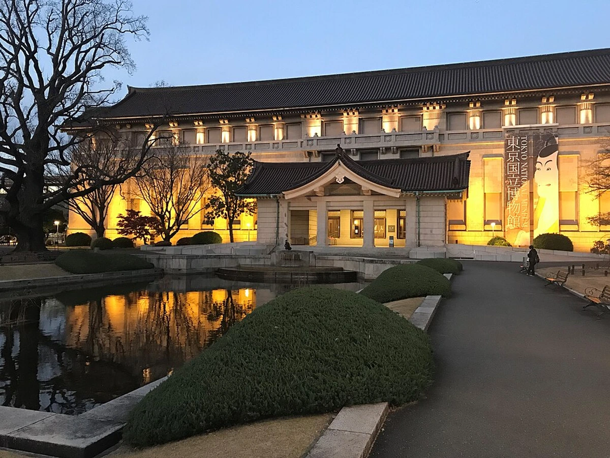 Exterior view of the Tokyo National Museum building and gardens at twilight, with lights reflecting in a pond.