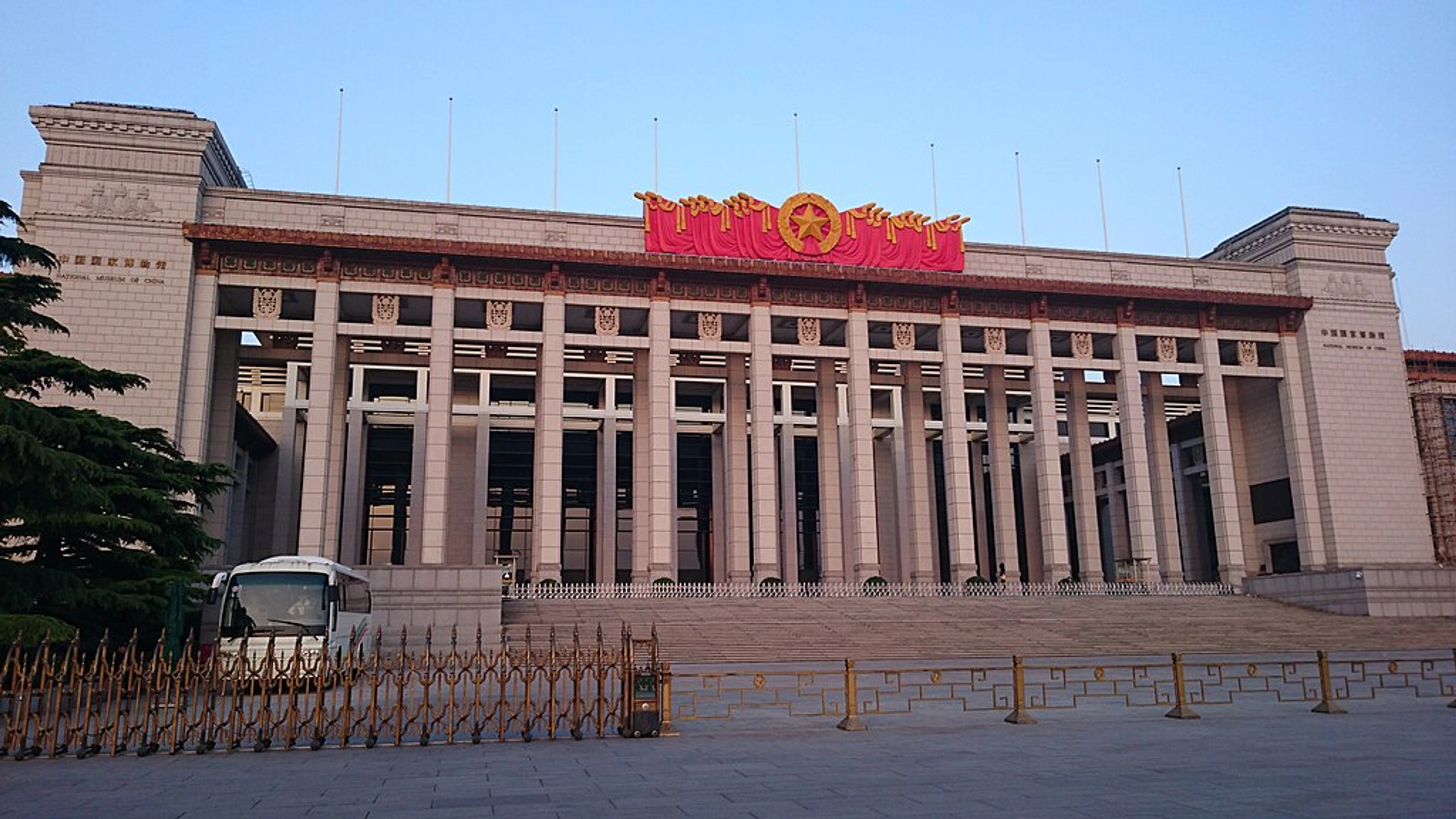 Frontal aanzicht van het gebouw van het Nationaal Museum van China in Peking, met de grote gevel, zuilen en een prominente banner met een sterembleem.