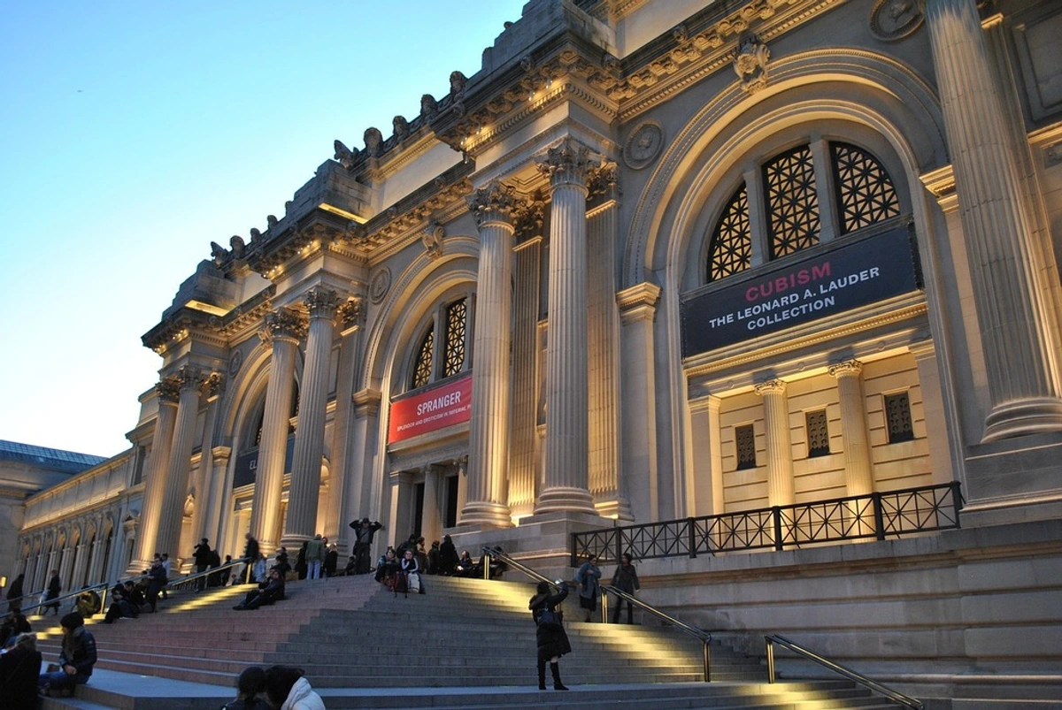 Evening view of the illuminated facade and grand staircase of the Metropolitan Museum of Art in New York City.