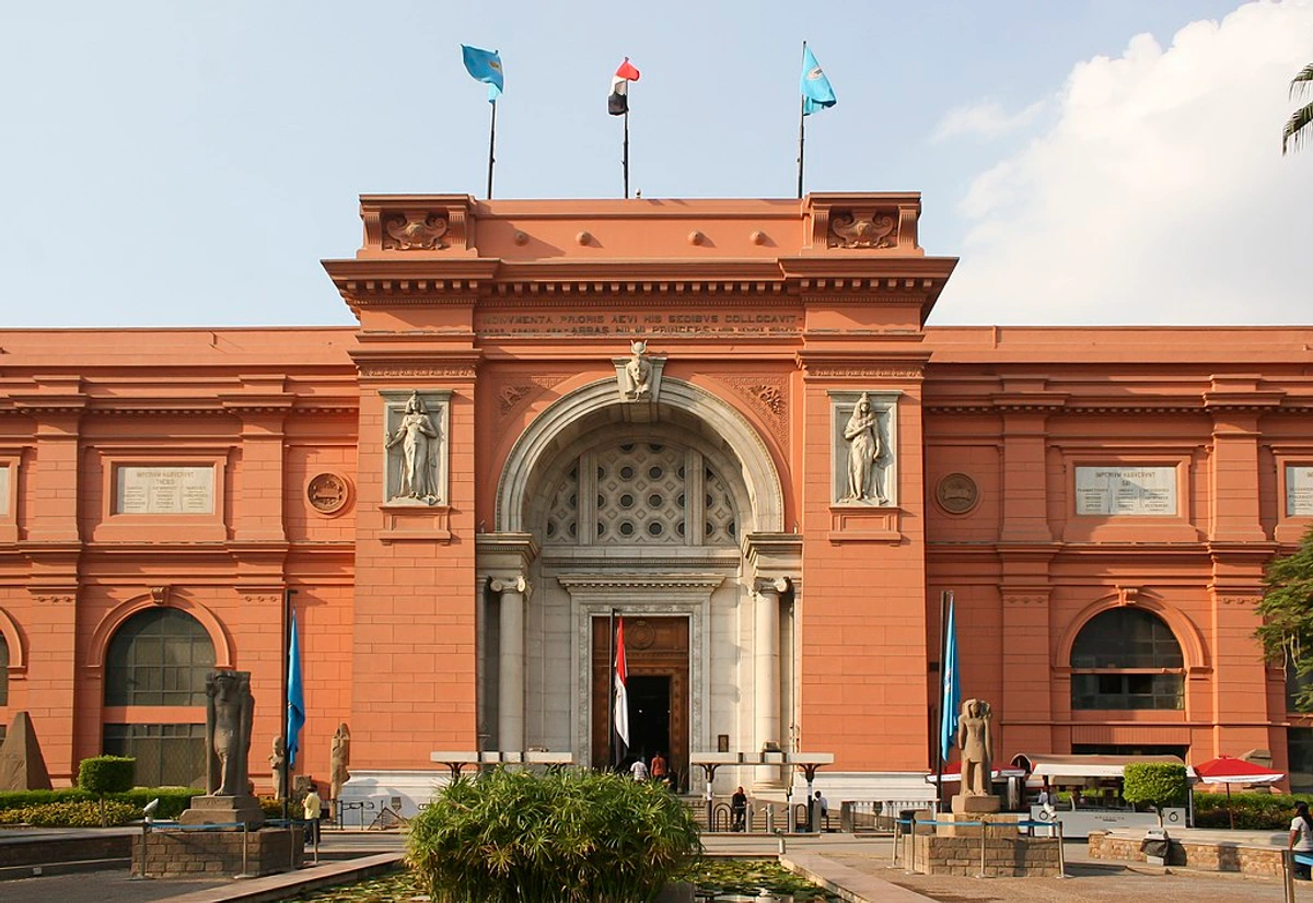 Frontal view of the Egyptian Museum in Cairo, featuring its grand entrance, statues, and flags flying on the roof.