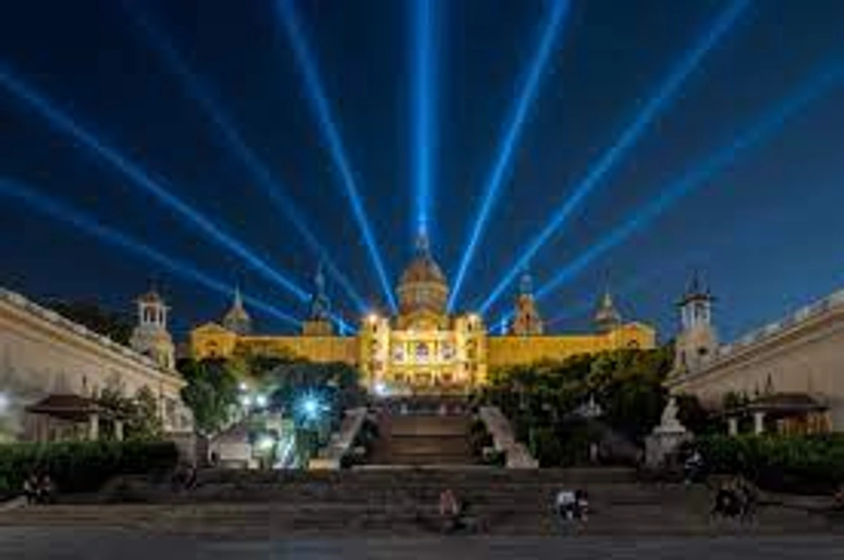 National Art Museum of Catalonia (MNAC) in Barcelona illuminated at night with blue light beams, viewed from the steps.