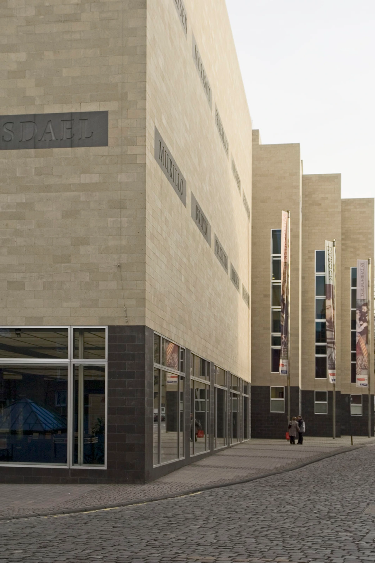 The modern stone facade of Museum Deventer in Deventer, Netherlands, featuring inscribed artist names like Murillo and Manet, large ground-floor windows, and a cobblestone street.