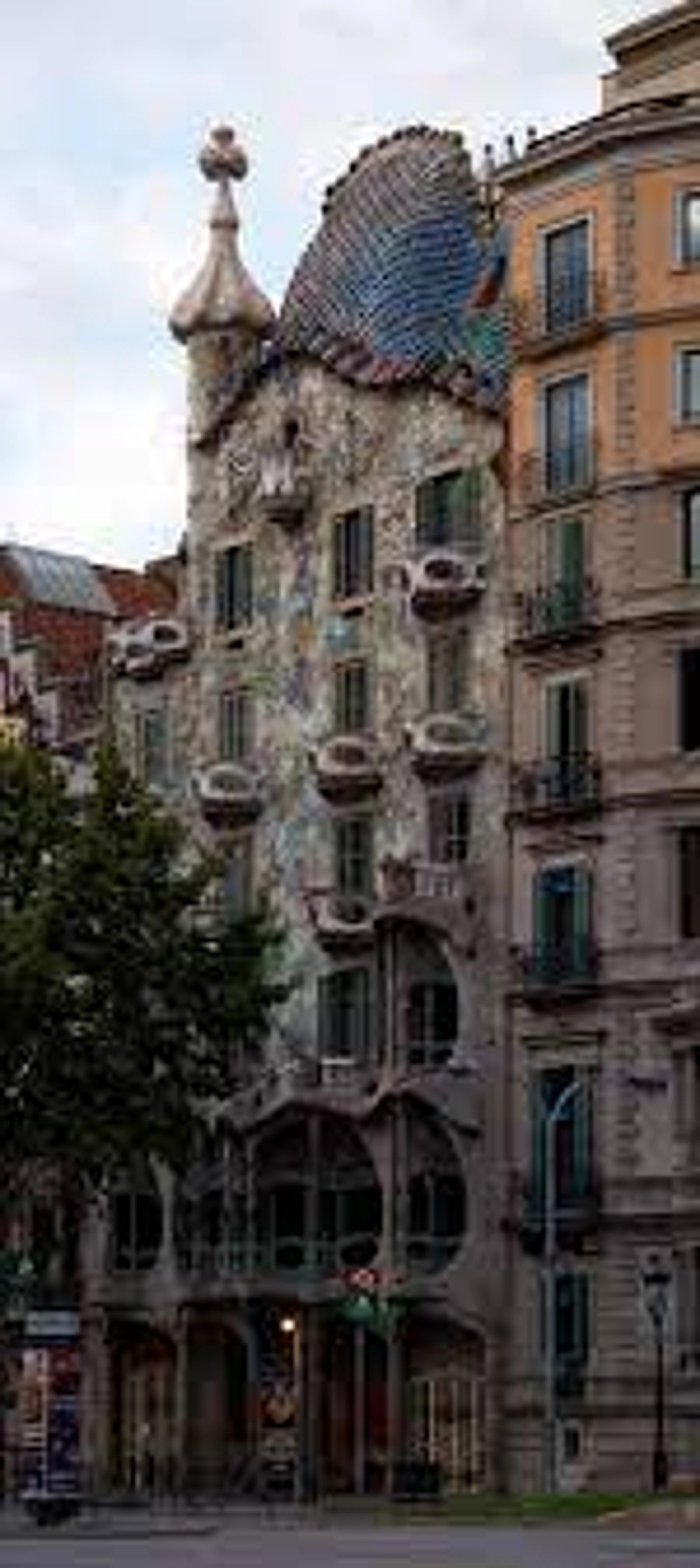 The unique facade of Casa Batlló by Antoni Gaudí in Barcelona, featuring organic shapes, colorful mosaic roof, and skull-like balconies.