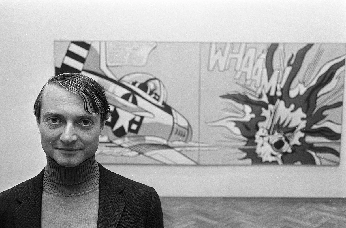 Zwart-witfoto van Roy Lichtenstein staand voor zijn iconische tweeluik schilderij "Whaam!", dat een straaljager afbeeldt die een raket afvuurt en een ander vliegtuig doet exploderen, met het onomatopee "WHAAM!" prominent weergegeven.