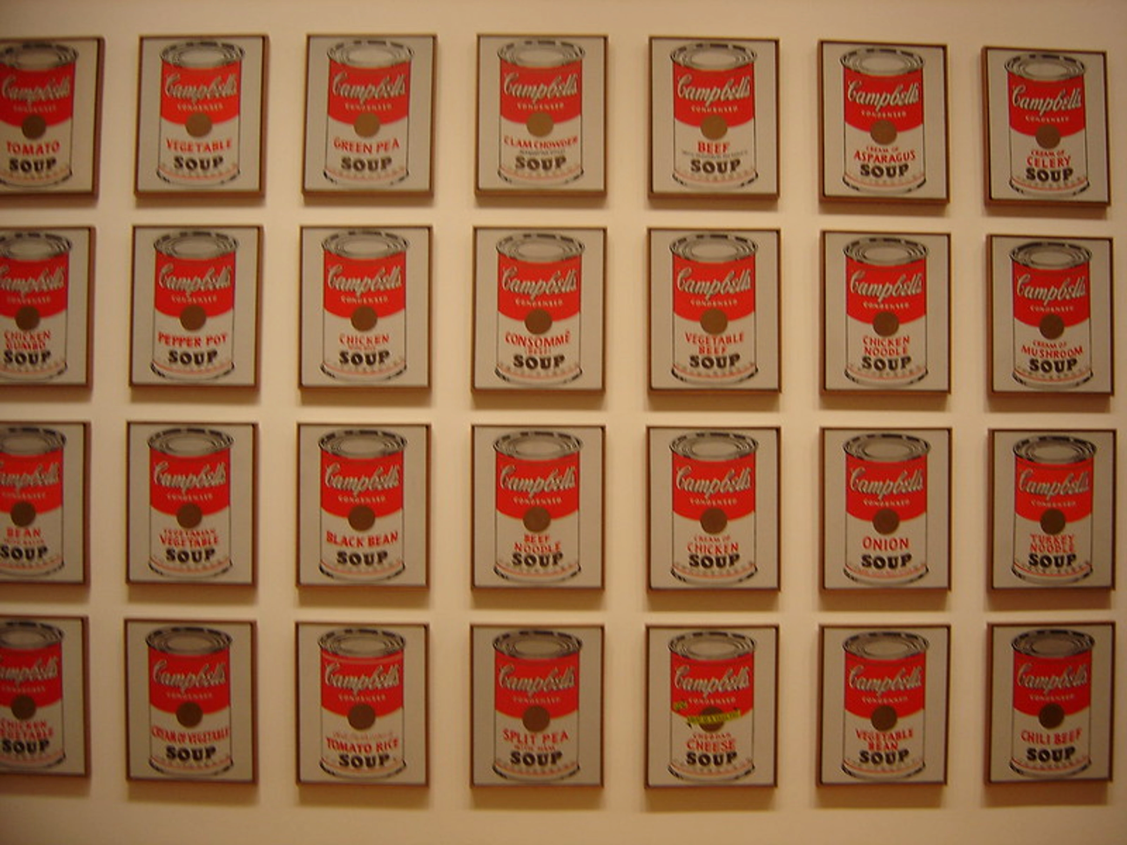 Raster van zeefdrukken van Andy Warhol met tweeëndertig verschillende soorten Campbell's Soup-blikken, elk afgebeeld in een eenvoudige, iconische stijl.
