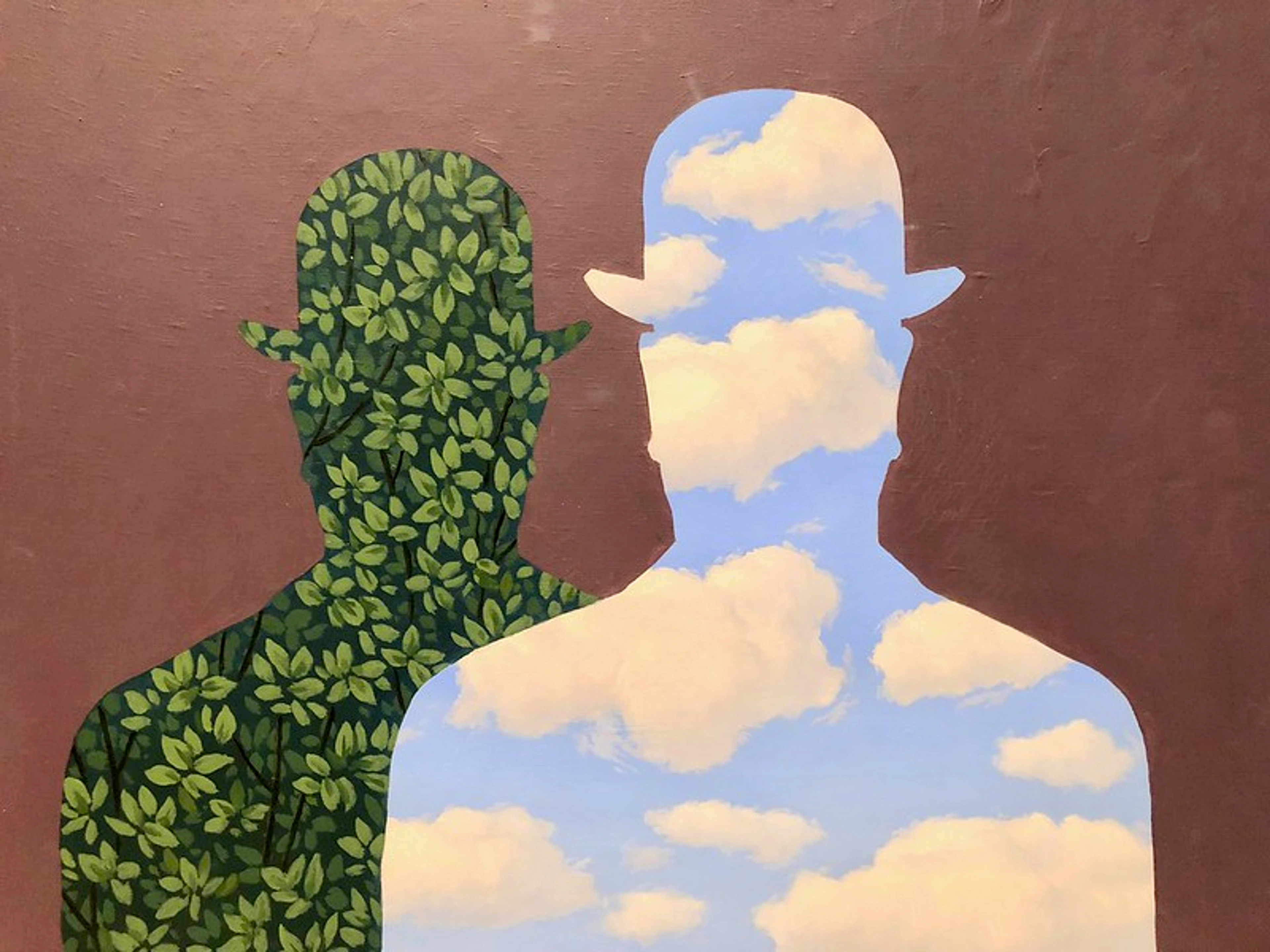 Surrealist painting by René Magritte featuring two silhouetted figures of men in bowler hats against a brown background. The figure on the left is filled with green leaves, while the figure on the right is filled with a blue sky and white clouds.