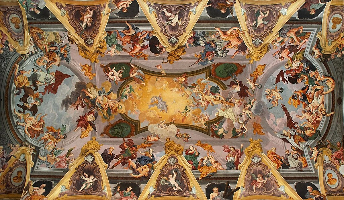 Intricate interior of a baroque church with white walls, ornate gold decorations, ceiling frescoes, and people seated in pews.