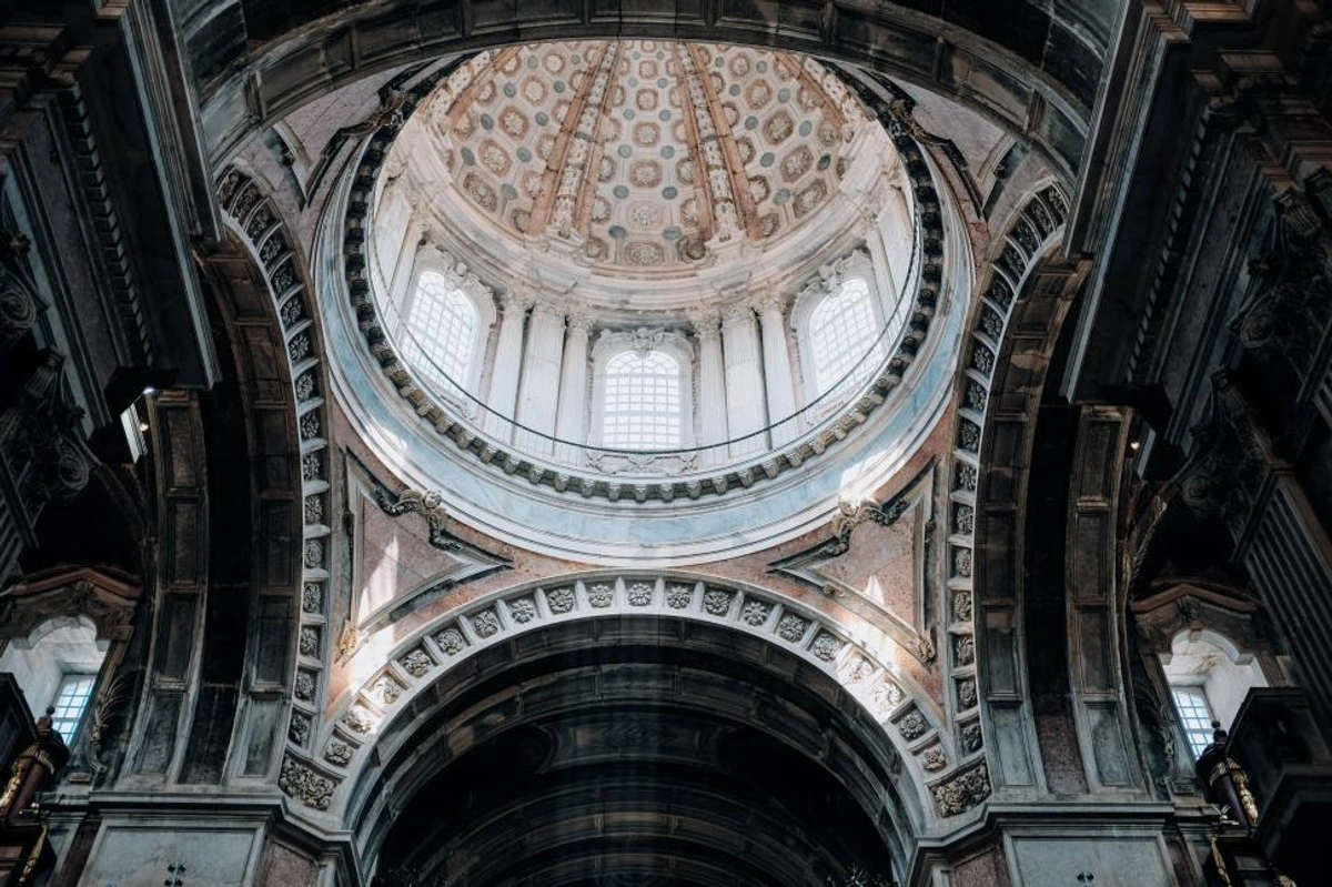 Interior view looking up at the ornate dome of the Santa Engrácia National Pantheon in Lisbon, Portugal, featuring intricate architectural details and patterns.