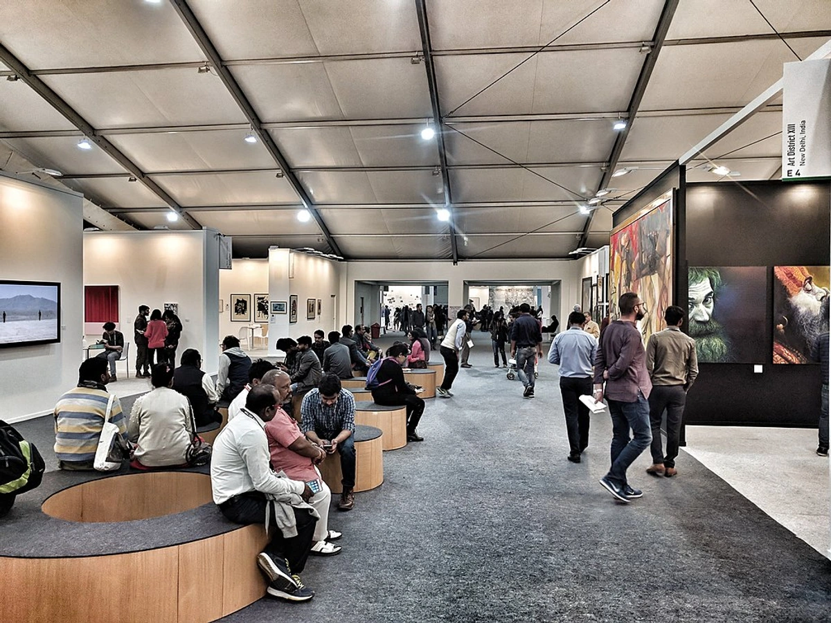 Interior view of a busy art fair with many people looking at various artworks displayed along the walls and in booths.