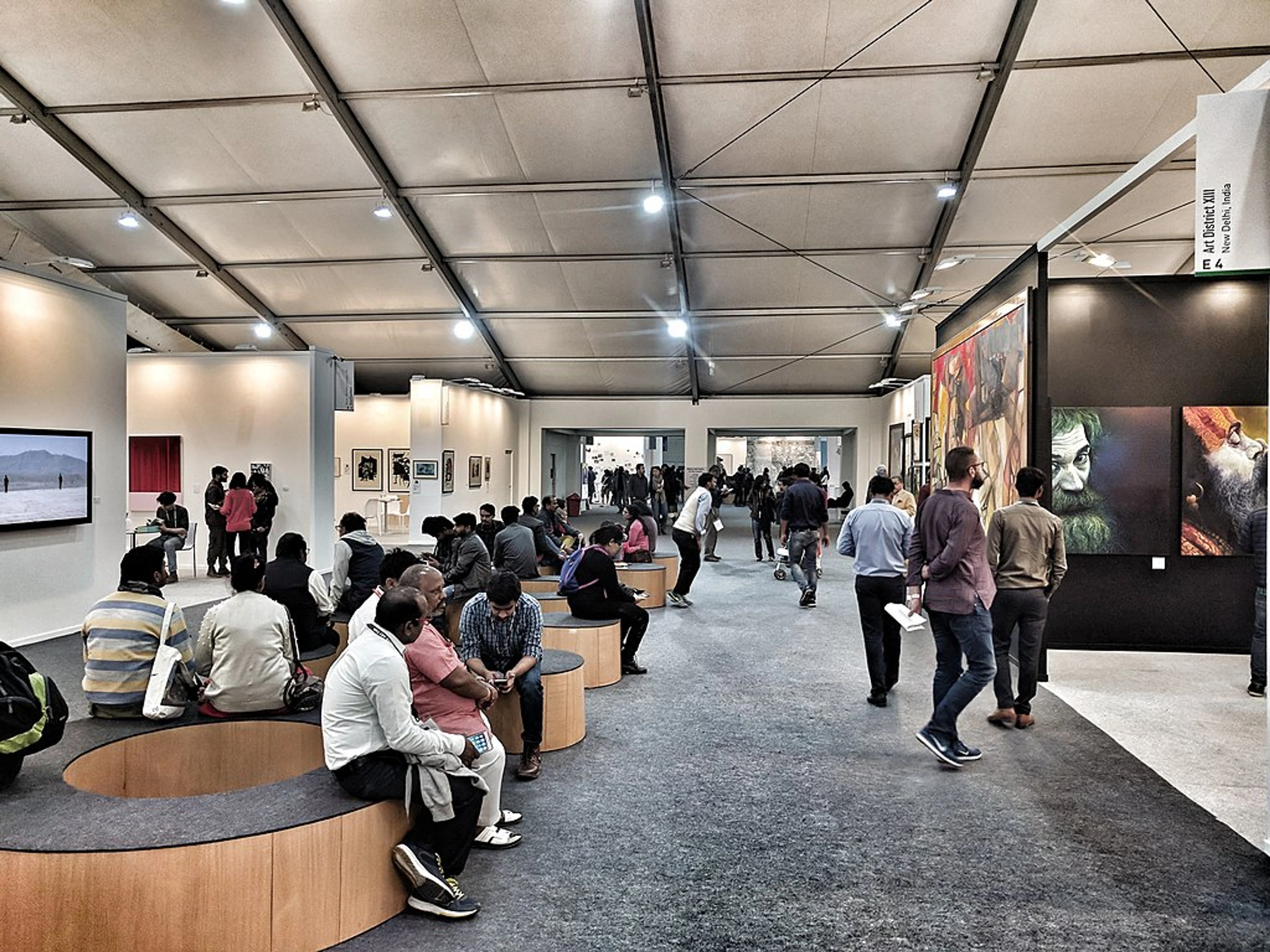 Interior view of a busy art fair with many people looking at various artworks displayed along the walls and in booths.