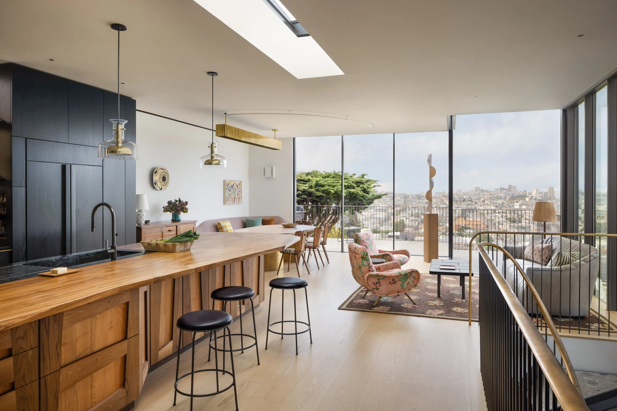 Interieur van een modern open-concept appartement met een keukeneiland, eetgedeelte en woonkamer met uitzicht op een stadsgezicht door grote ramen.