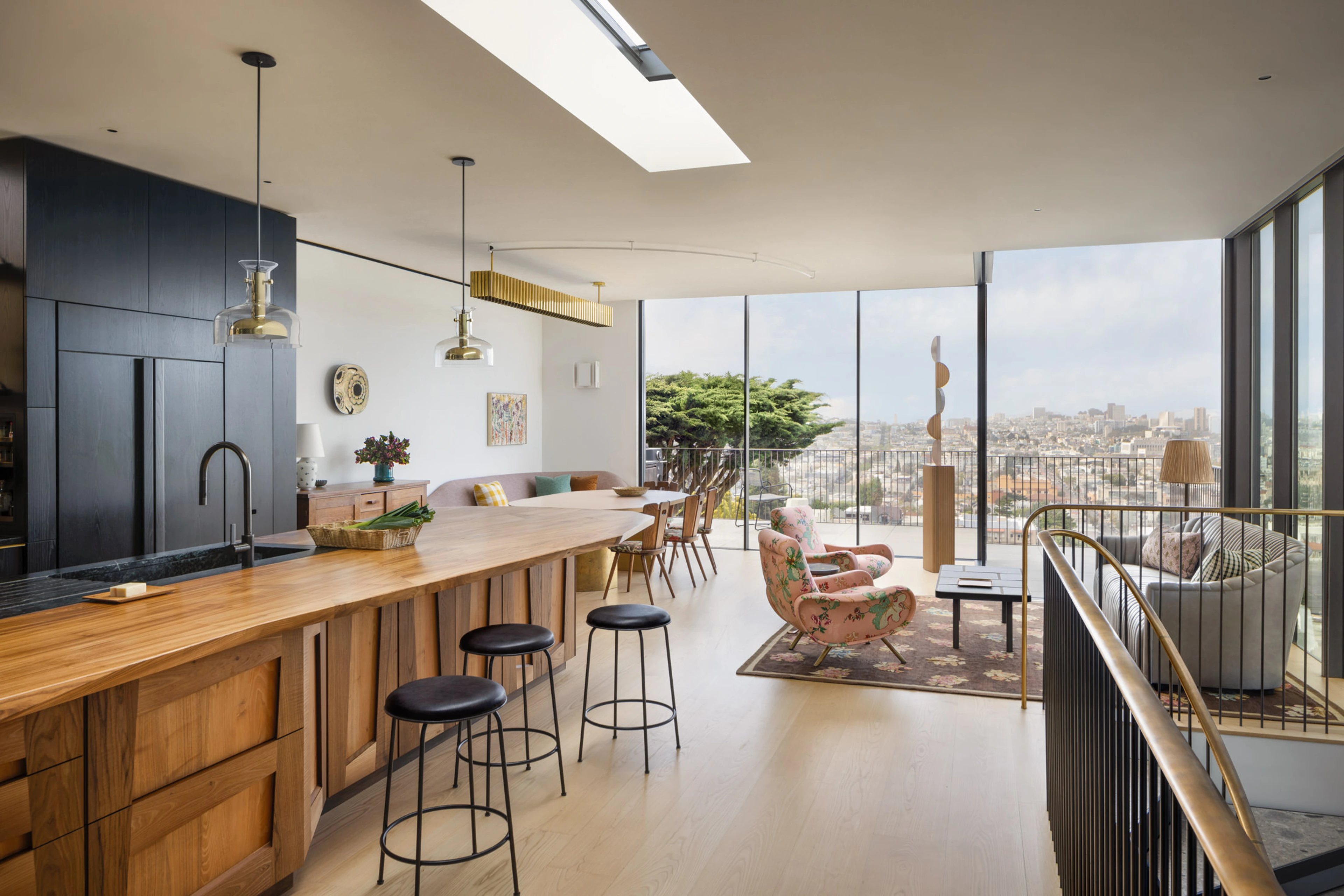Interieur van een modern open-concept appartement met een keukeneiland, eetgedeelte en woonkamer met uitzicht op een stadsgezicht door grote ramen.