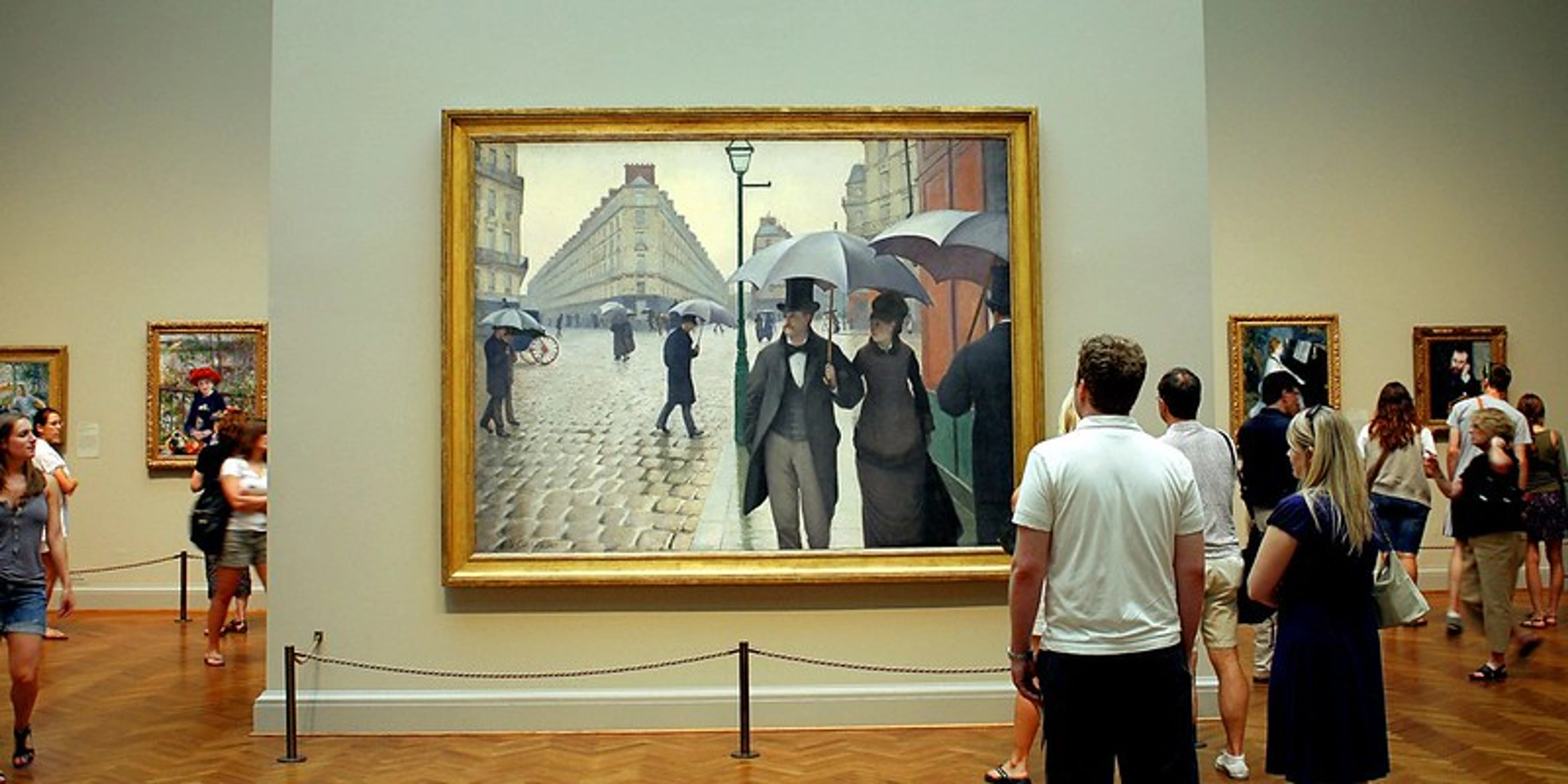 Museum visitors viewing Gustave Caillebotte's "Paris Street; Rainy Day" in a gallery setting.