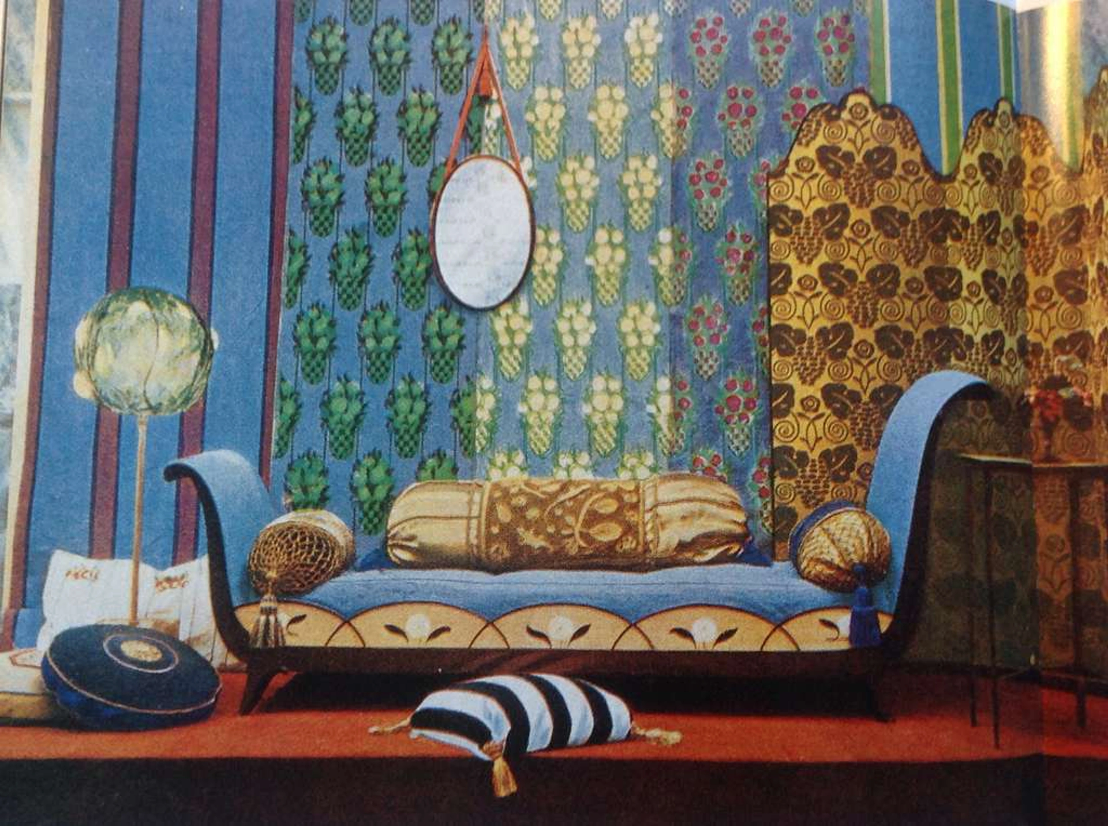 An Art Deco styled interior with a blue curved sofa, patterned wallpaper, decorative pillows, and a hanging oval mirror.