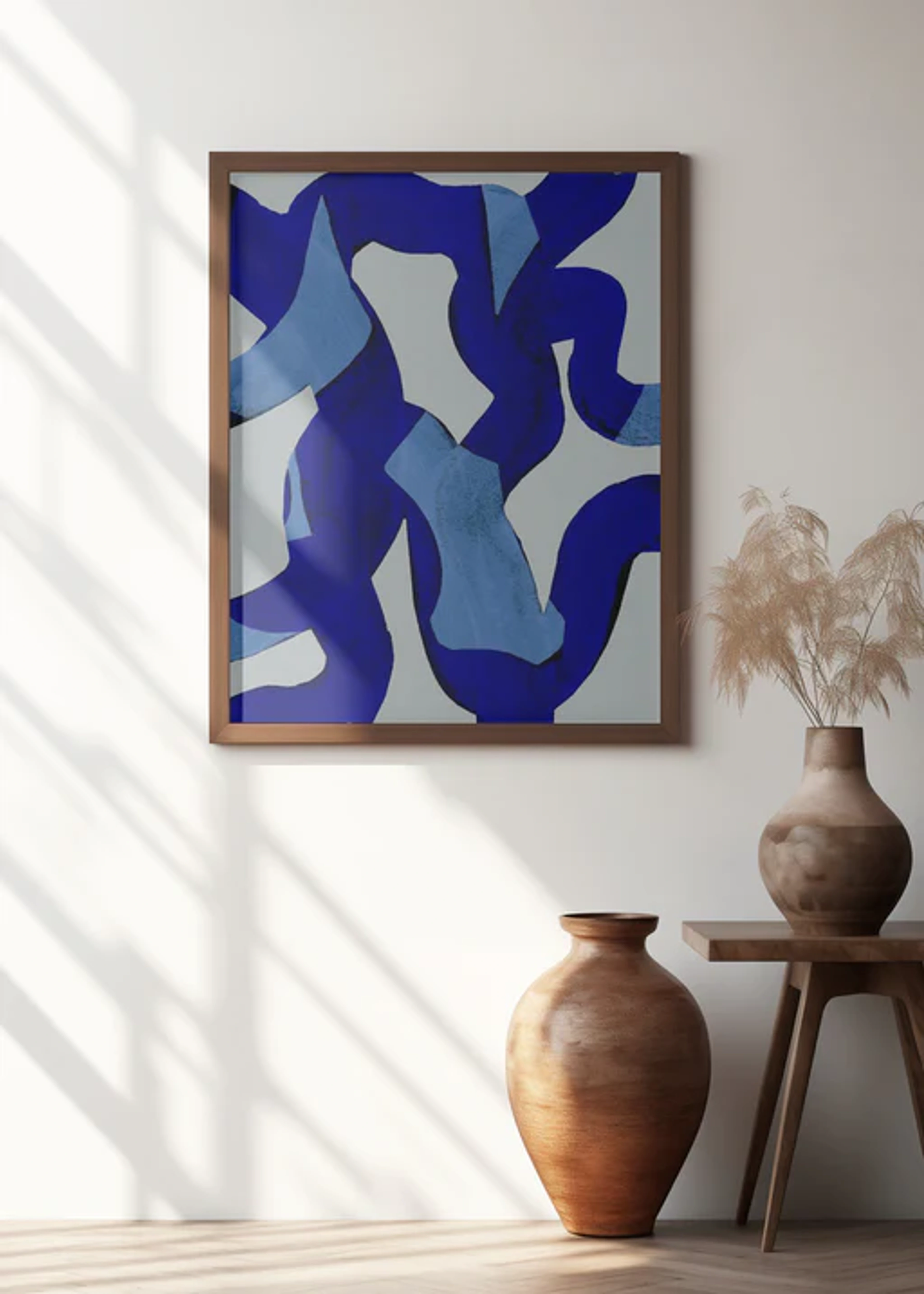 Ingelijste abstracte schilderij met gedurfde blauwe penseelstreken op een lichtgrijze achtergrond, hangend aan een witte muur boven twee bruine vazen op een houten tafel.