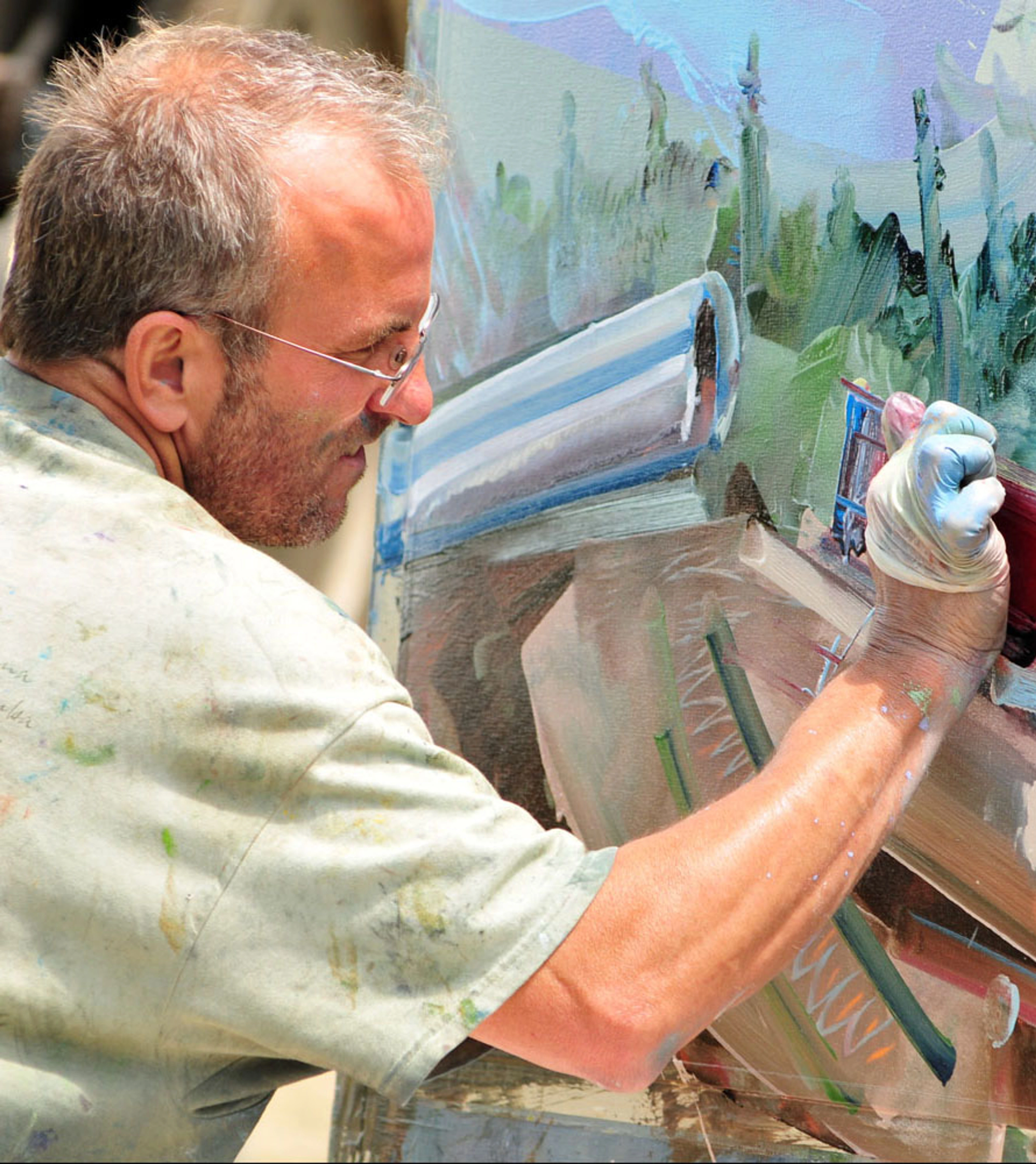 Close-up of painter David Brewster focusing intently on a canvas outdoors, using a palette knife with blue paint