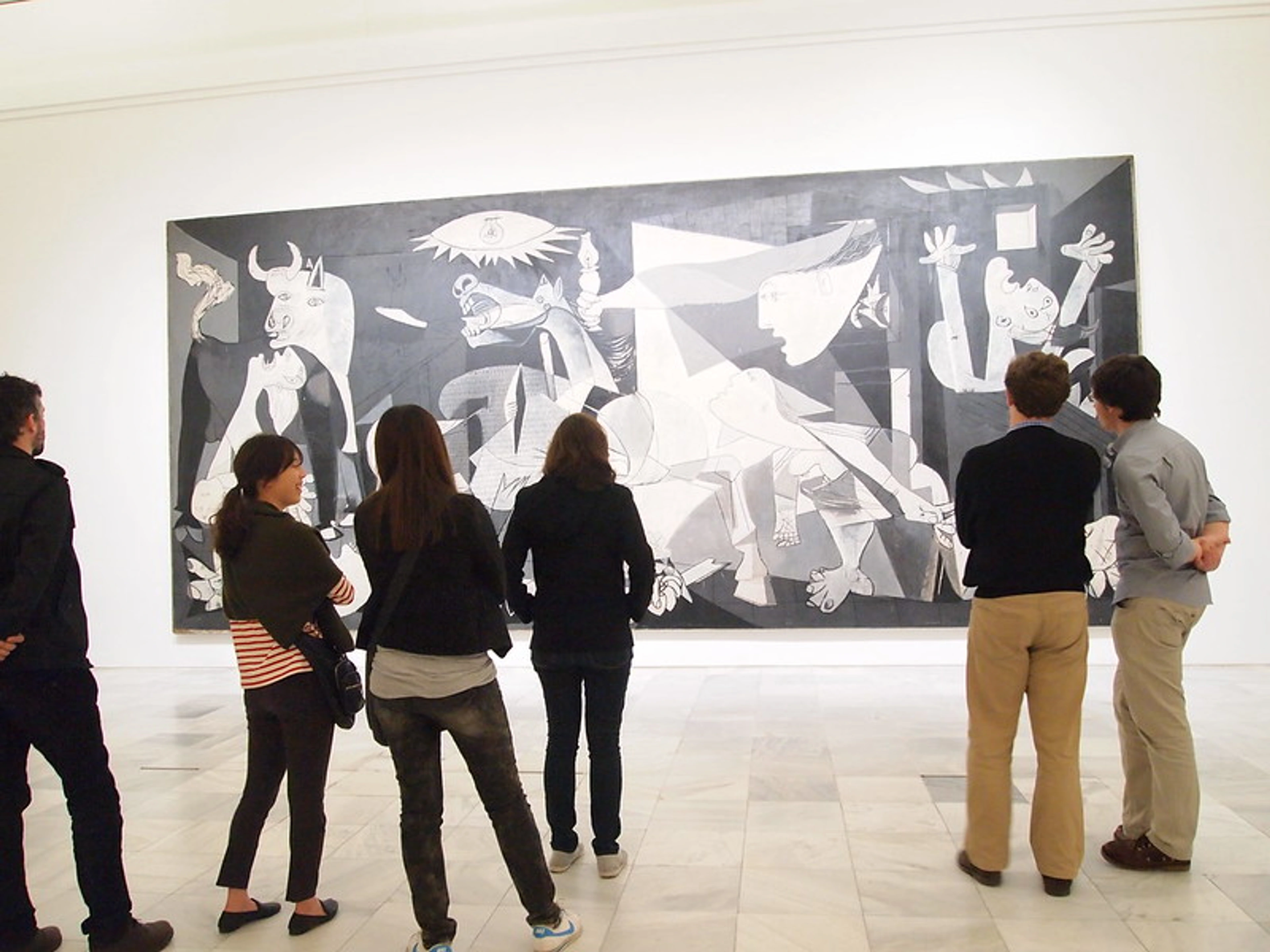 Museum visitors observing Pablo Picasso's large black and white painting "Guernica" in a gallery.