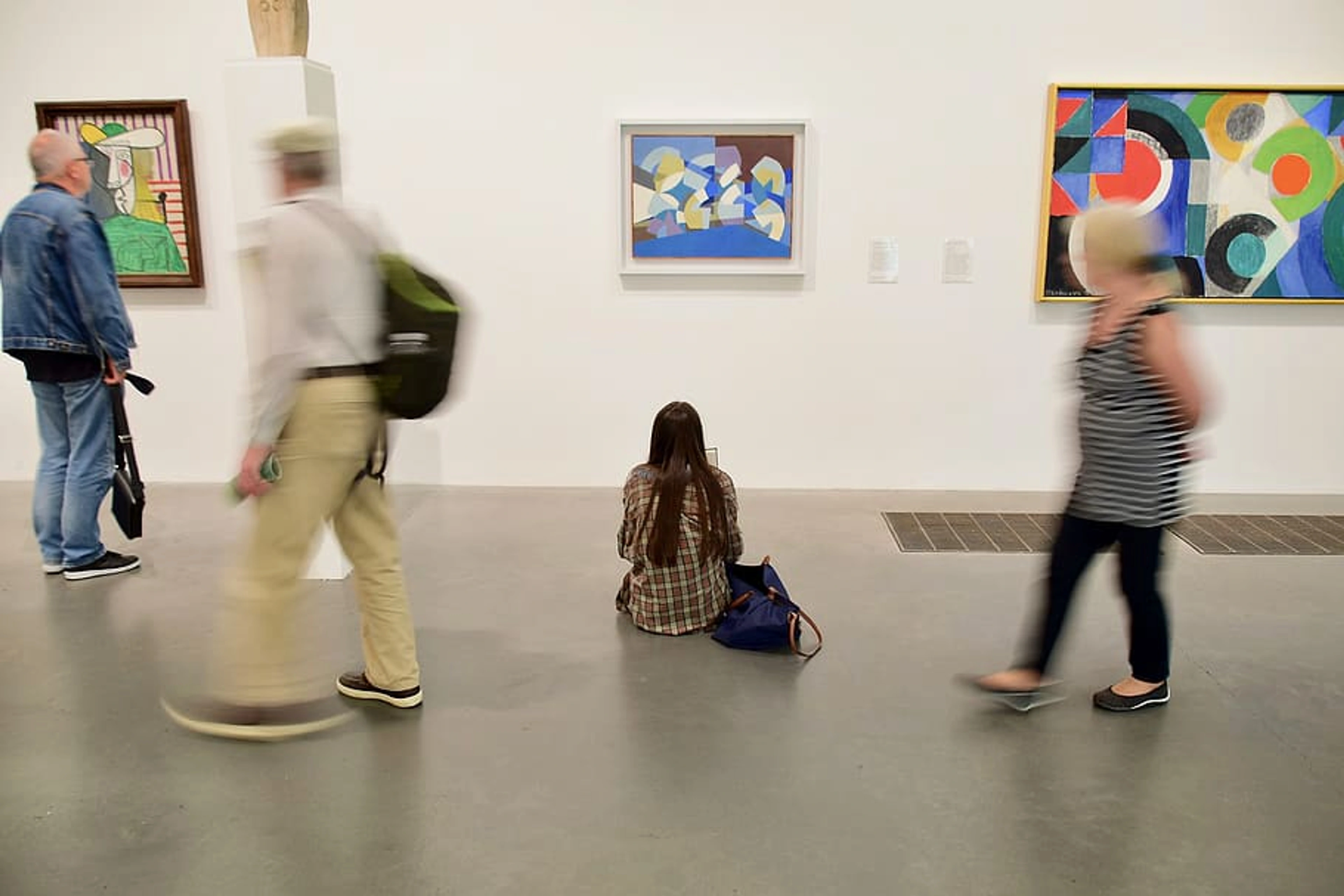People viewing modern art paintings in a white-walled gallery.