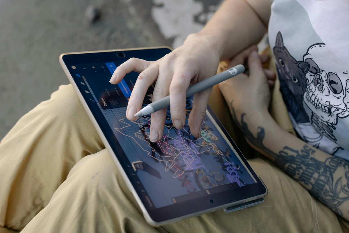 A person's hands using a stylus pen on a drawing tablet, with a digital illustration visible on the screen.