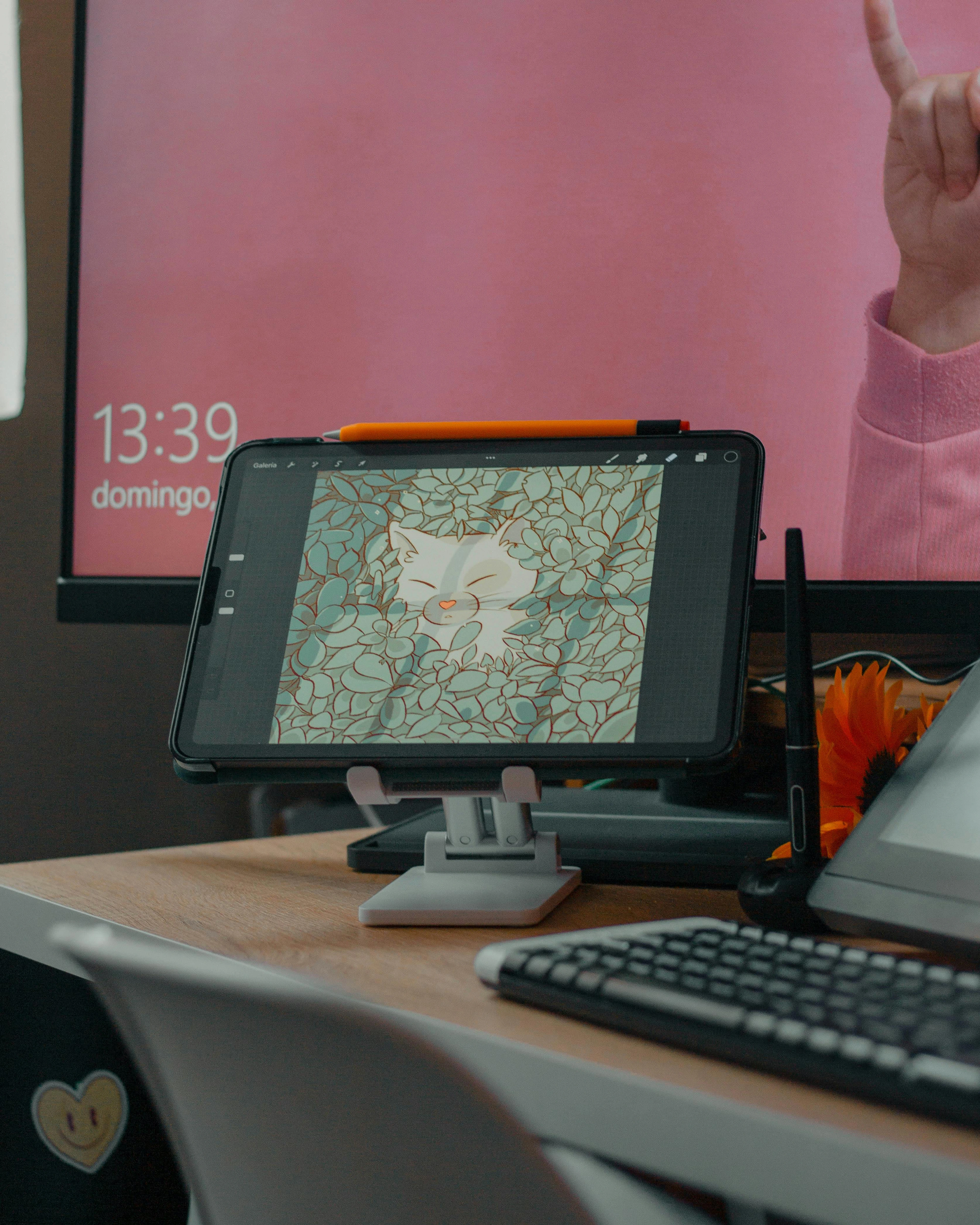 Digital artist's workspace with a drawing tablet displaying a cat illustration, an orange stylus, and a keyboard on a wooden desk.