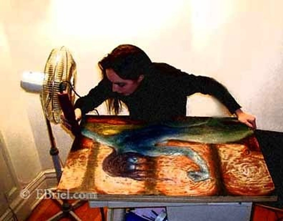 Artist working on an encaustic painting with a fan blowing on it.