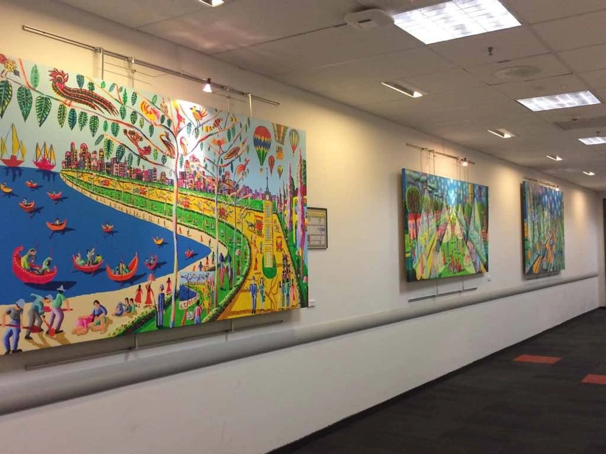 Levendige naïeve kunsttentoonstelling met kleurrijke schilderijen van stadsgezichten, boten en mensen in een gang.