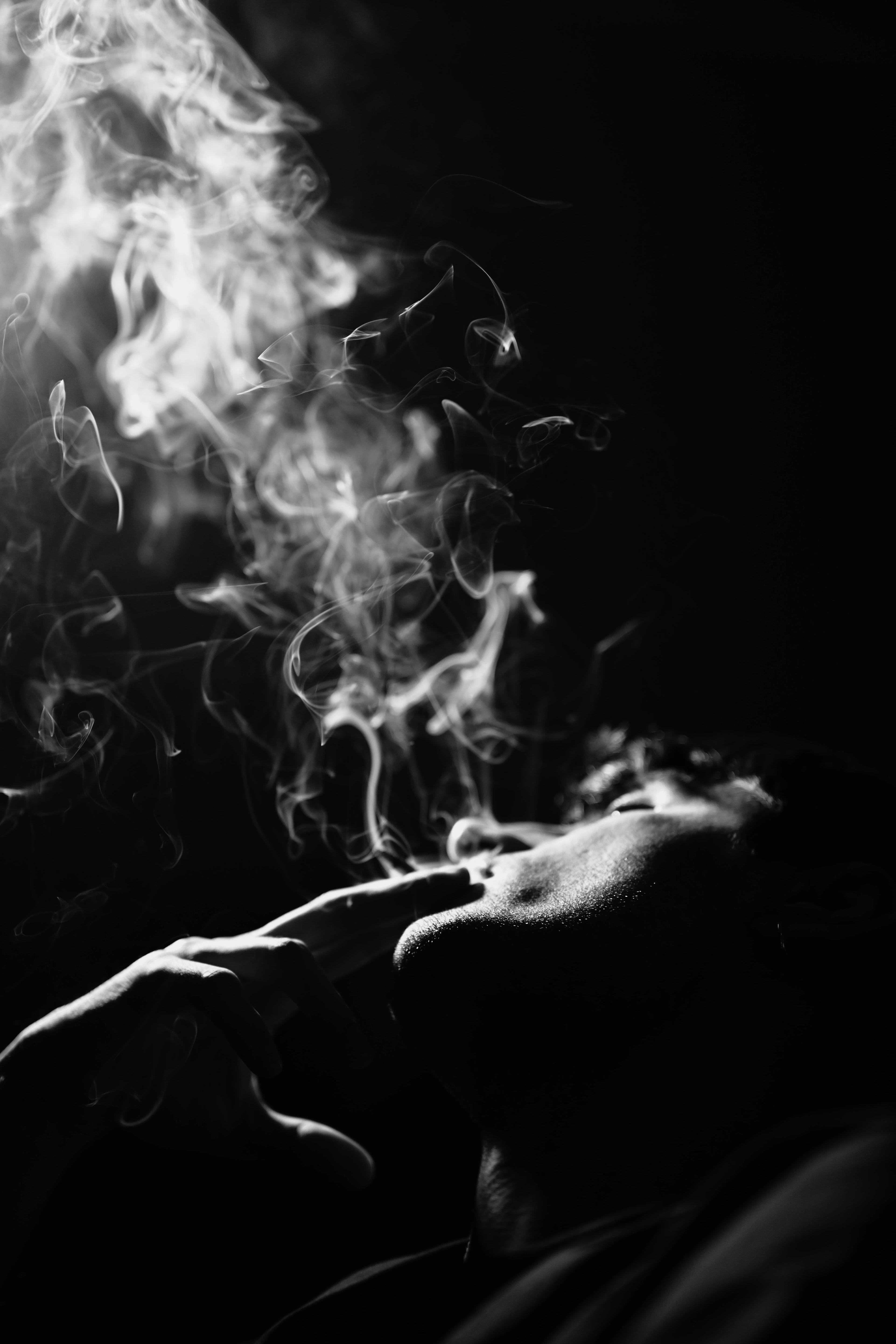 Abstract black and white photo of a man exhaling cigarette smoke, dramatic lighting.